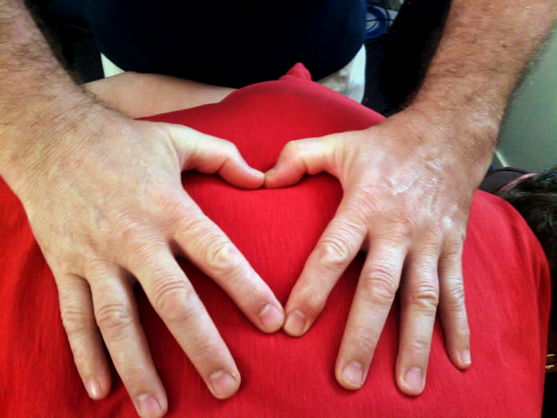 Stewart Gatenby performing Bowen Therapy on a client with a red shirt. Stewart's hands form a heart shape