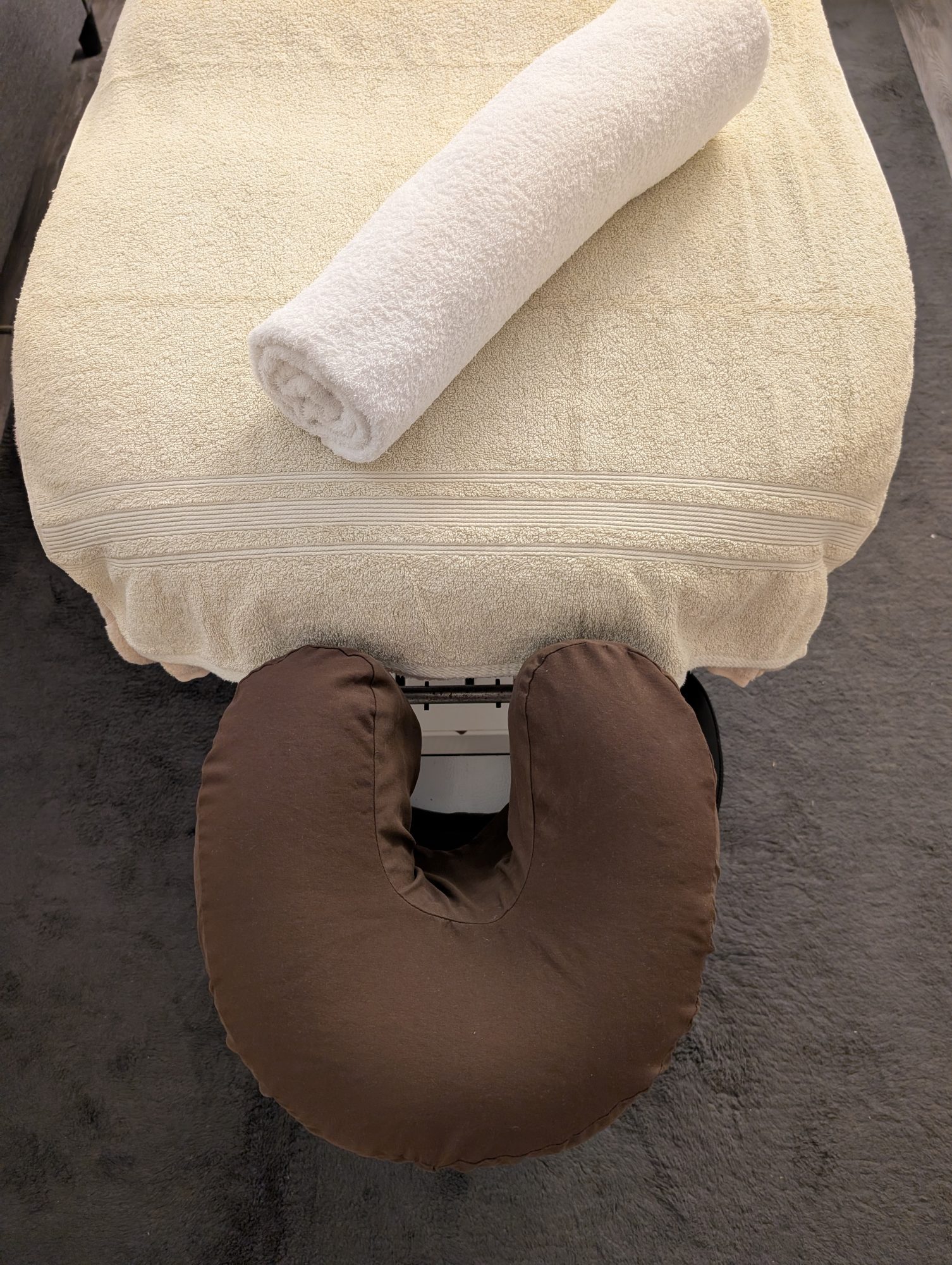 Massage table in the clinic room at Breathe Easy Bowen & Massage, set with a cream towel and brown headrest topped with a rolled-up white towel