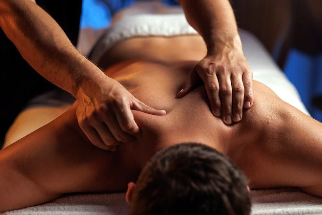 Hands massaging a man whilst he is lying on a massage table, head towards the camera