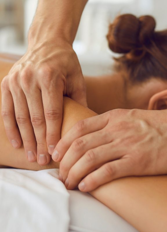 Hands massaging a woman's shoulder whilst she is lying on a massage table