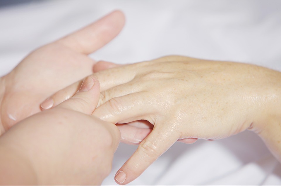 Female Caucasian hand massaging another female Caucasian's fingers, whilst holding the hand being massaged, a white background.