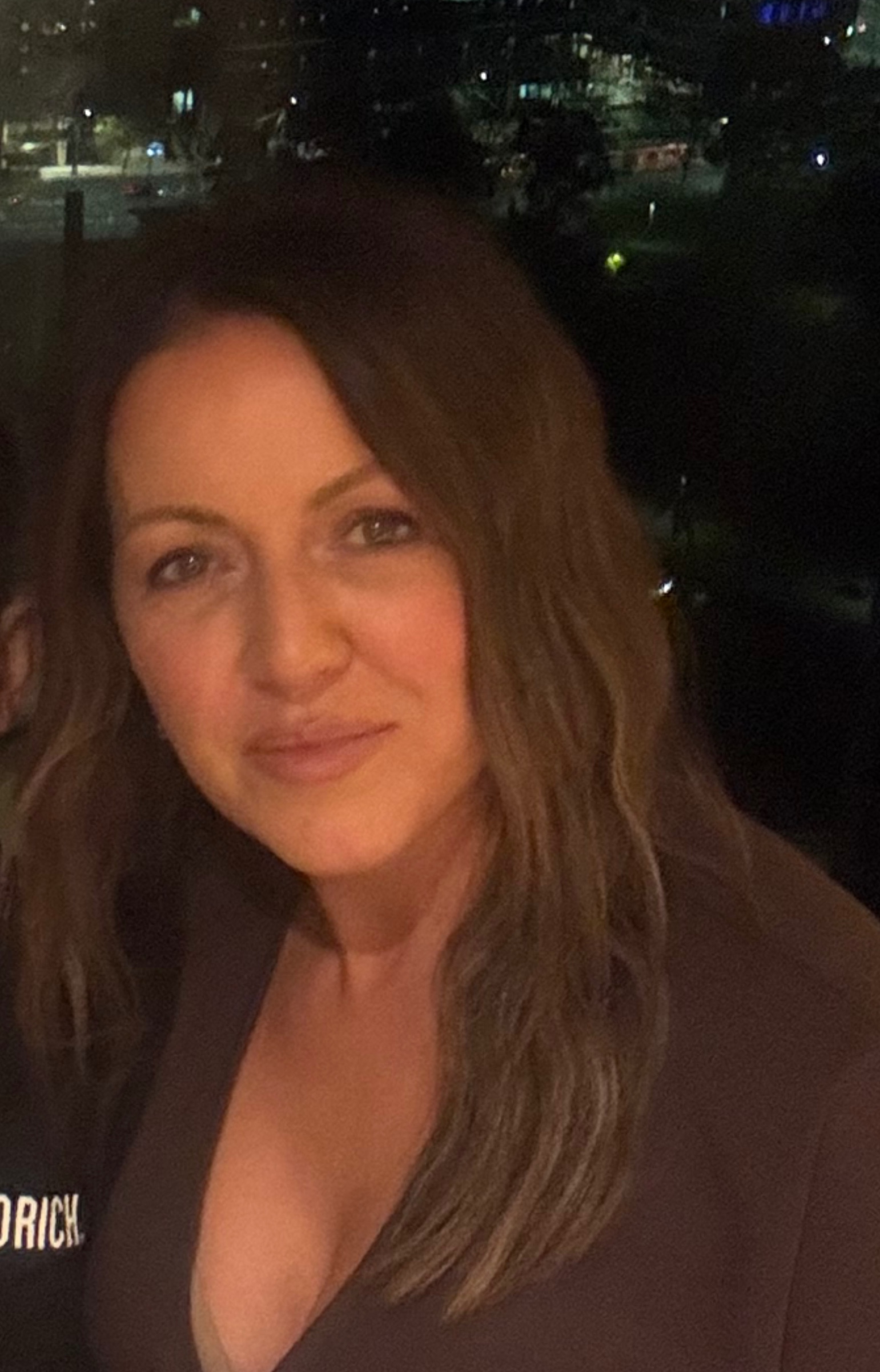 Angie Pascuzzi, homeopath, head shot, wearing a brown top with brown hair and dark window in the background