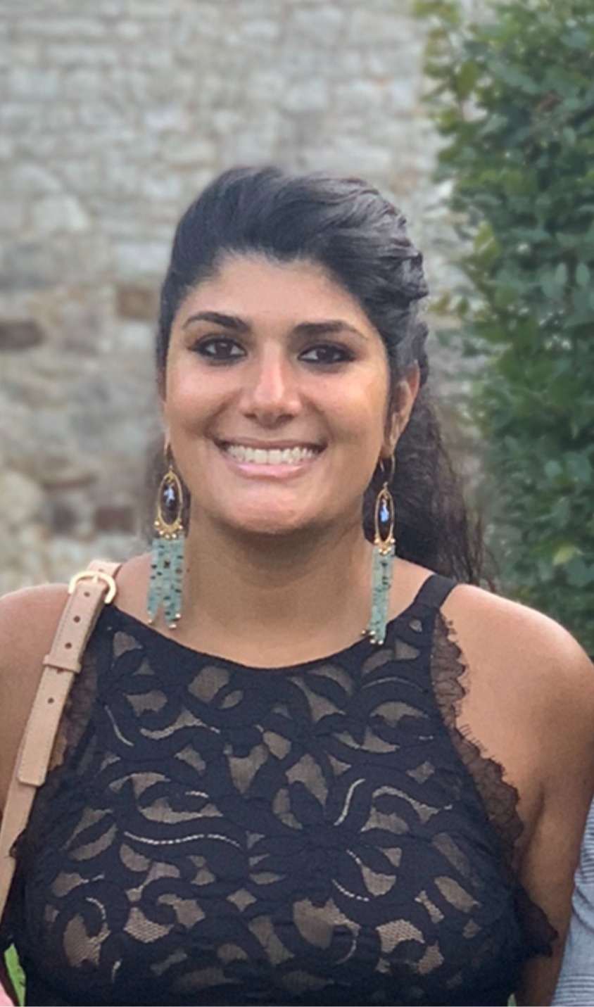 Heda Breece, wearing long green beaded and pearl earrings, wearing black dress. Smiling and has a dark tan and black hair in a pony tail.